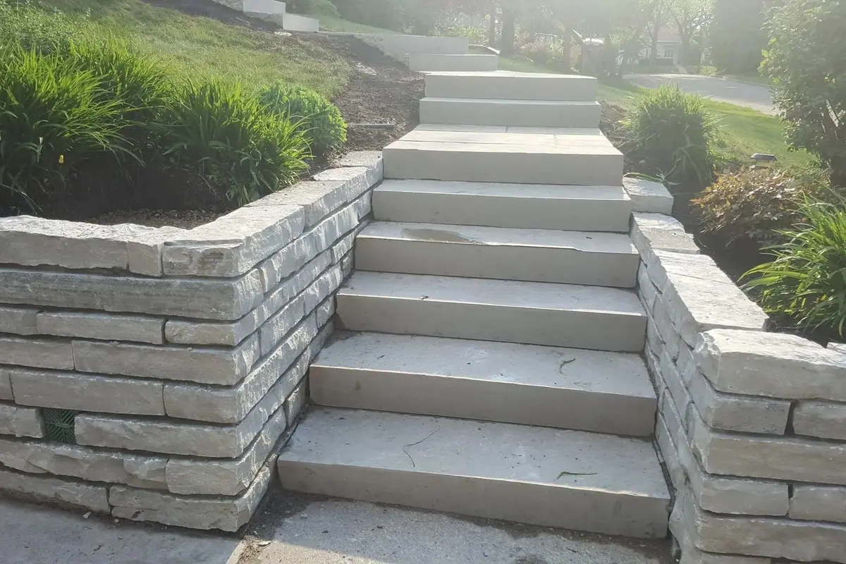 Escalera de piedra entre muros de contención que sube por un jardín